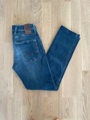 Blå Replay Anbass jeans W30 - Jag säljer dom här riktigt snygga blå Replay Anbass jeansen som är i storlek W30. De är upplagda så utgå ifrån måtten. Dom är i fint skick utan skador. Tveka inte att höra av er!                 Mått:  Längd=95cm Midja=36cm