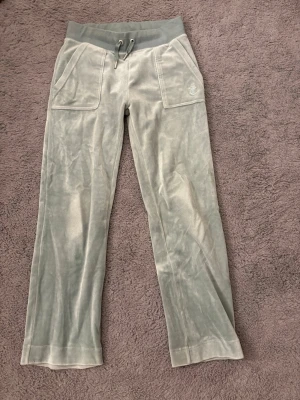 Ljus gröna  Juicy Couture XS - mjukisbyxor från Juicy Couture med bred resårmidja och snörning. Byxorna har stora fickor fram, bakfickor med knappar och ett broderat JC-logo på ena fickan.  Använt fåtal gånger