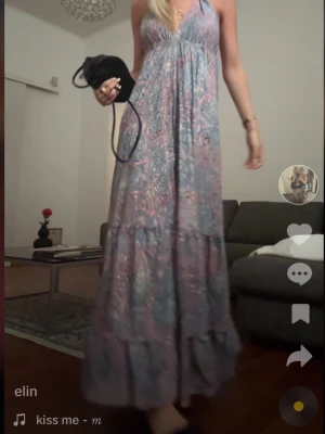 Lång blommig klänning med omlott - Säljer en superfin långklänning med blommigt mönster i ljusa toner av lila, rosa och blått. Klänningen har omlott-design, v-ringad hals och tunna axelband. 