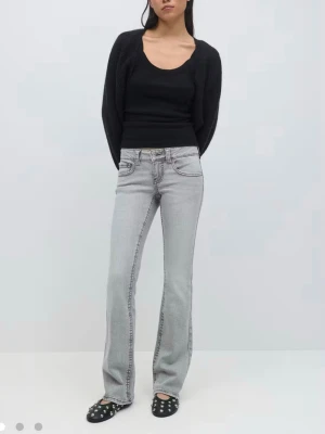 Grå bootcut jeans med fickdetaljer - Snygga ljusgrå jeans med bootcut-snitt och coola fickor med lock och knapp bak. Jeansen har låg midja och klassisk femficksdesign. Perfekta för dig som gillar en avslappnad men ändå trendig look. Materialet är mjukt jeans och färgen är lätt tvättad grå. Inköpta för 500kr