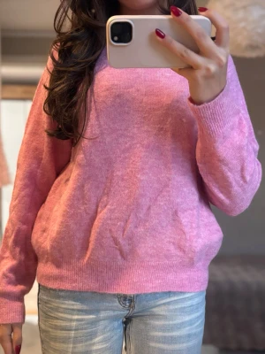 Rosa stickad tröja med rund hals - Säljer en mjuk och mysig rosa stickad tröja med rund hals och långa ärmar. Tröjan har ribbade muddar vid ärmslut och nederkant, perfekt för att hålla värmen under kyliga dagar. Passar dig som gillar en avslappnad och bekväm stil.