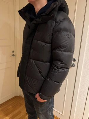 Svart Moncler madeira down jacket - Säljer min moncler madeira jacket då den blivit lite liten. Materialet är glansigt och känns riktigt lyxigt, perfekt för kalla dagar. Passformen är normal och jackan är långärmad. Modellen är 190 och väger ca 85 kg. Pris går att diskutera🙌