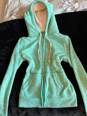 Mintgrön hoodie - Säljer en söt mintgrön hoodie från SO. Tröjan har vit snörning i huvan, mysigt teddyfoder på insidan av huvan och praktiska fickor framtill. Materialet är stickat och mjukt, med ribbade muddar vid ärmslut och nederkant. Perfekt för att piffa upp outfiten!💕 