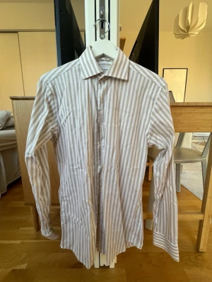 Randig skjorta från John Henric - Klassisk skjorta med vertikala ränder i ljusblått och vitt. Skjortan har lång ärm, knappar framtill och en stilren krage. Perfekt för dig som gillar en clean och tidlös look. Tillverkad i bomull för en skön känsla hela dagen. OBS: Bilden med modellen är i samma färg men samma modell för att visa passform. 