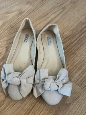 Beige ballerinaskor med rosett - Snygga beige ballerinaskor från NLY Shoes i mjukt material med rund tå och stor dekorativ rosett framtill. Skorna har en klassisk och enkel design som passar till många olika outfits. Perfekta för dig som gillar en feminin och stilren look.