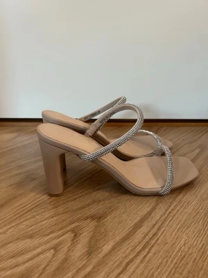 Bal klackar  - Säljer ett par snygga beige klackar från Amisu med fyrkantig tå och bred klack. Remmarna är dekorerade med glittriga stenar som ger extra bling. Skorna har öppen tå med mjuk innersula. De är endast testade inomhus. Köpta på new yorker