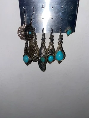 Silver örhänge med turkosa stenar  - Bilderna visar ett gäng örhängen i silverfärg med turkosa stenar. Fick allt från min moster. Andvänd 3-10 gånger max. Bara gamla inte smutsiga. 6 par och ett ensam örhänge. 50kr men kan sänka till önskad pris. 