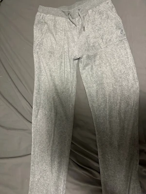 Grå mjukisbyxor från Juicy Couture - Grå mjukisbyxor från Juicy Couture med snörning i midjan och två fickor fram samt två bakfickor med knapp. Byxorna har en relaxed passform och är tillverkade i mjukt bomullsmaterial. Perfekta för chill dagar eller när du vill vara extra bekväm. Köpte dom på kidsbrandstore skulle säga den passar s  den saknar en sån sak på snöret 