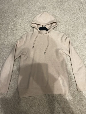 Merino Ull Hoodie - En god och skön hoodie i merino ull, beige den edna deffekten är att den har slits upp lite vid kragen med har sytts på. 