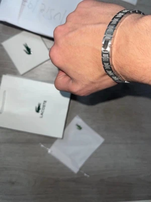  Silver Lacoste armband Metropole  - Stilrent armband från Lacoste i silverfärg. Kommer med original ask, påse, dammpåse och certifikat. Perfekt accessoar för att lyfta din outfit med en modern touch. Justerbar storlek 
