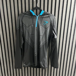 Ingen sko på bild - Bilderna visar en långärmad hoodie med mönster och blå detaljer, men ingen sko finns med.