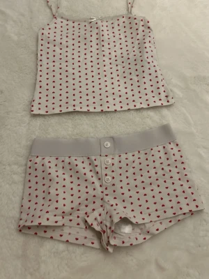 Vit pyjamas med röda hjärtan - Söt vit pyjamas med tunna axelband och små röda hjärtan över hela tyget. Den har en rak passform och är gjord i mjuk bomull, perfekt för en avslappnad look. Matcha med shorts för en gullig pyjamasstil.🫰🏼