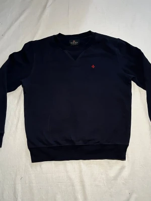 Svart tröja från Morris - Svart tröja från Morris i storlek S. Tröjan har en klassisk rund halsringning med ribbade muddar och en liten röd broderad detalj på bröstet. Mjuk insida och stilren design. Kontakta oss vid minsta fundering eller fråga!✅🙂