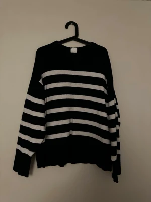 Marinblå randig stickad tröja - Säljer en marinblå stickad tröja med breda vita horisontella ränder. Tröjan har rund halsringning, långa ärmar och en relaxed fit. Lite nopprig och börjar bli dålig i vita färgen