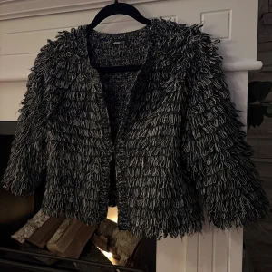 Svart och grå stickad cardigan jacka - Unik stickad cardigan jacka från Gina Tricot i svart och grått med coola fransdetaljer över hela ytan. Jackan har långärmad design och en loose passform som ger en avslappnad vibe. Perfekt för dig som vill sticka ut med din stil.