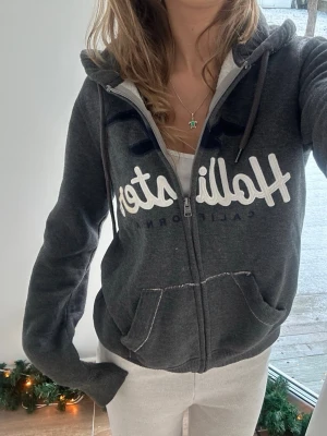Hollister zip - En zip från Hollister i storlek XS, kan upplevas större i storlek, likt en S. Finns en fläck på loggan men går nog bort i tvätt eller med vanish. Jag fraktar inom 24h. Se liknande plagg i min profil!