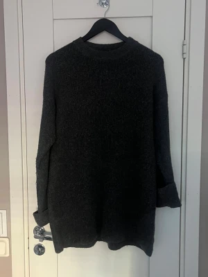 Mörkgrå stickad tröja med lång ärm - Mysig mörkgrå stickad tröja med rund hals och långa ärmar. Tröjan har en loose passform och är perfekt för kyliga dagar. Materialet är grovstickat och ger en skön känsla. Ärmarna kan vikas upp för en avslappnad look.