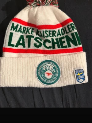 (Oanvänd) Vit Latschenkiefer mössa från Afterski team - Vit stickad mössa från Marke Kaiseradler med grön och röd text runtom, broderad patch framtill och färgglad tofs på toppen. Mössan har vikt kant och Team Sweden-märke på sidan. Perfekt för afterski och vinterhäng. Oanvänd med nypris 349! Kom gärna med bud!