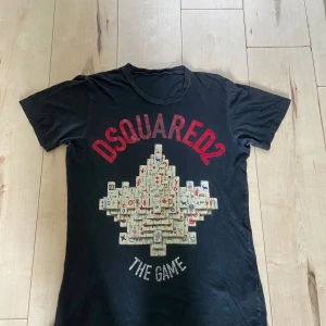 Svart DSQUARED2 t-shirt med print - Svart t-shirt från DSQUARED2 med stort grafiskt print på framsidan och röd logga. Modellen är kortärmad och har rund hals. Materialet är mjuk bomull och passformen är normal. Perfekt för dig som gillar statement-plagg och coola designer.