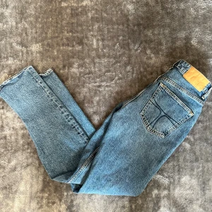 Blå raka jeans med hög midja - Klassiska blå jeans med raka ben och hög midja. Jeansen har en snygg vintage-look, fem fickor och tydliga kontrastsömmar. Materialet är robust denim i bomull. Perfekta för en avslappnad och tidlös stil.