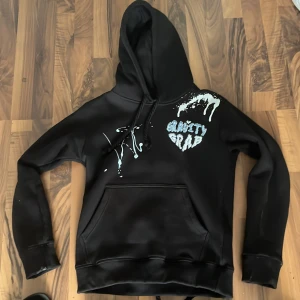Svart hoodie Gravity Grab med tryck - Svart hoodie från Gravity Grab med stor huva och känguruficka. Framsidan har vitt och blått tryck med texten 'Gravity Grab' och coola färgstänk. Baksidan har GG-tryck i blått och vitt. Perfekt för dig som gillar streetwear och unika detaljer. Kom med bud snälla 🙏 