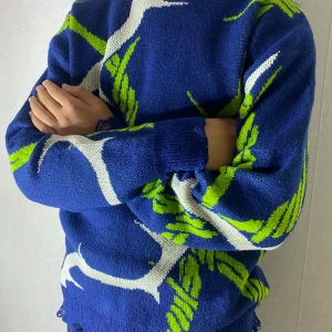 Blå stickad tröja med taggtrådsmönster - Säljer en blå stickad tröja med grönt och vitt taggtrådsmönster. Tröjan har lång ärm, rund halsringning och coola slitna detaljer längst ner. Perfekt för dig som vill sticka ut med en edgy vibe.