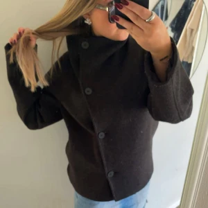 Svart kappa  - Säljer denna fina kappa i 158-164. Jackan har en rak passform, bred krage och knäppning med stora knappar framtill. Perfekt nu till hösten