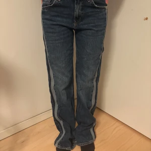 Blå jeans med ljusa sidor från Zara - Snygga blå jeans från Zara med raka ben och ljusare panel längs sidorna. Klassisk femficksmodell med hög midja och kontrastsömmar. Jeansen är i kraftigt denimtyg och har en cool, avslappnad vibe. Perfekta för dig som gillar en unik twist på klassiska jeans. Använda fåtal gånger