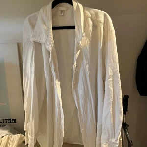 Vit oversized skjorta från H&M XL - Luftig och oversized vit skjorta från H&M i storlek XL. Skjortan har en avslappnad passform, klassisk krage och knäppning framtill. Tillverkad i ett lätt och strukturerat bomullstyg som ger en chill vibe. Perfekt att styla lager på lager eller bära som den är.