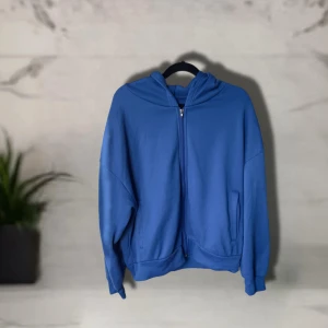 Blå hoodie med dragkedja, storlek L - En blå hoodie i storlek L med dragkedja framtill och två fickor. 