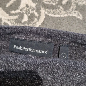 Mörkgrå stickad tröja Peak Performance - Snygg mörkgrå stickad tröja från Peak Performance i storlek L. Tröjan har en klassisk rund hals och långärmade raglanärmar. Materialet är mjukt och ger en chill vibe, perfekt för att hålla värmen under kyliga dagar. Diskret logga nertill på framsidan. Pris kan diskuteras.