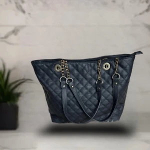 Svart quiltad axelväska med kedjedetaljer - Stilren svart axelväska i quiltat skinnimitation med guldfärgade kedjor och detaljer. Väskan har dragkedja upptill, innerfack och ett extra fack med dragkedja på baksidan. Perfekt storlek för att få plats med allt du behöver. Snygg och trendig design.