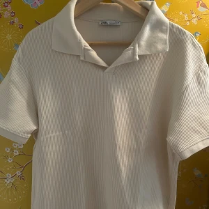 Vit pike från Zara  - Säljer en ribbad vit piké t-shirt från Zara i storlek M. T-shirten har korta ärmar, klassisk krage och är tillverkad i mjuk bomull. Perfekt för en clean och chill stil med snygg struktur tack vare ribbningen.