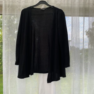 Svart kofta från KappAhl - En svart, tunn och enkel kofta från KappAhl i storlek 146/152. Koftan har lång ärm och öppen front, perfekt att slänga över en t-shirt eller linne. Stilren och passar till det mesta, med mjukt och lätt material. Passar XS/S