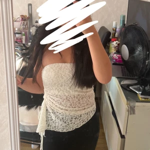 Vit spets tubtopp med snörning - Säljer en vit axelbandslös tubtopp i spets med snygg snörningsdetalj på sidan. Toppen har ett feminint blommigt spetsmönster och är lätt transparent. Perfekt för dig som vill ha en trendig och somrig look. Använd 1 gång, från new yorker i strl S