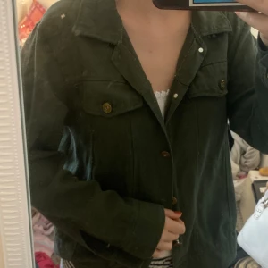 Mörkgrön jacka med guld detaljer  - Snygg mörkgrön jacka i jeans/manchester med krage och bröstfickor med knappar. Använd få gånger så är i fint skick men lappen är bortklippt och det saknas en knapp på ärmen 💕