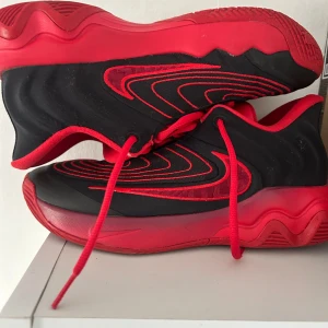 Nike sneakers svart/röd strl 40 - Säljer ett par riktigt snygga Nike sneakers i svart och rött med coola vågformade detaljer på sidorna. Skorna har snörning, rund tå och en tjock, vågig röd sula. Ovandelen är i syntetmaterial och mesh för bra andningsförmåga. Perfekta för dig som gillar sportig stil.