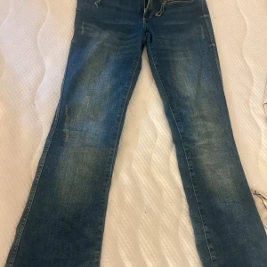 Blå bootcut jeans från H&M - Snygga blå bootcut jeans från H&M med justerbar midja och låg midja. Klassisk femficksmodell i mjukt denimtyg med lätt slitning och raka ben som går ut lite nertill. 