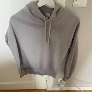 Grå hoodie från H&M i storlek S - Enkel och stilren grå hoodie från H&M i storlek S. Tröjan har huva med snörning och ribbade muddar vid ärmslut och nederkant. Perfekt för en avslappnad look och passar till det mesta. Mjuk och skön med klassisk passform.