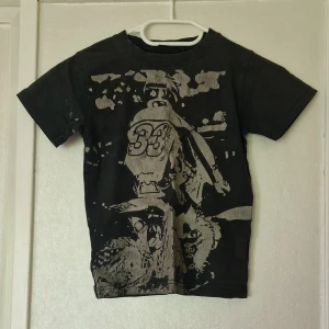 Svart t-shirt med motorcykeltryck - Svart t-shirt med ett stort tryck av en motorcyklist och siffran 33 på framsidan. T-shirten har korta ärmar och en klassisk passform. Materialet känns som bomull och trycket ger en rå streetkänsla. Perfekt för dig som gillar motorsport eller vill ha en edgy look. Det är mycket sprickor i trycket.