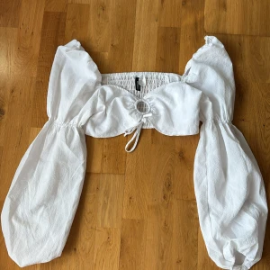 Vit croppad blus med puffärmar - Superfin vit croppad blus från H&M med stora puffärmar och knytning framtill. Toppen har en rund detalj i mitten och resår i ryggen för skön passform🌼