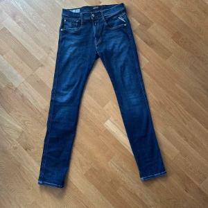 Replay Anbass 31/32 - Snygga Replay Anbass jeans i mörkblå tvätt med klassisk femficksdesign och vita kontrastsömmar. Modellen har raka ben, normal passform och tydlig Replay-logga på bakfickan. Tillverkade i stretchig bomullsdenim för skön känsla hela dagen.