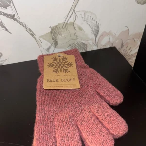 Rosa stickade handskar från Falk Sport - Mysiga stickade handskar i en dämpad rosa nyans från Falk Sport. Perfekta för kalla dagar, med klassisk design och ribbad mudd. Materialet är mjukt och värmande, och handskarna har en enkel, tidlös look.