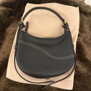 ATP Silea - Kommer med dustbag och bandet. Snygg svart axelväska i skinn från ATP Atelier med rundad form och kontrasterande vita sömmar. Väskan har både kort handtag och lång justerbar axelrem med guldfärgade metalldetaljer. Perfekt storlek för det viktigaste och stilren design.