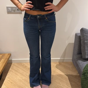 Blå bootcut jeans med låg midja - Snygga blå jeans med bootcut passform och låg midja. Klassisk femficksmodell med guldfärgade sömmar och dragkedja. Jeansen är i ett mjukt denimtyg som sitter tajt över låren och släpper ut vid vaden för en riktigt schysst siluett.