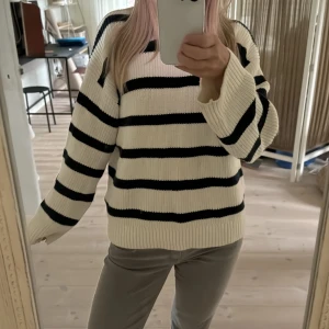 Randig stickad tröja i vitt och svart - Säljer en oversized stickad tröja med breda svarta ränder på vit botten. Tröjan har lång ärm, rund hals och ribbade muddar. Perfekt för dig som gillar en chill och trendig look.
