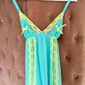 Turkos spetsklänning Victoria's Secret - Supersöt turkos kortklänning från Victoria's Secret med ljusgula spetsdetaljer och små rosetter framtill. Klänningen har tunna axelband och är tillverkad i ett lätt, transparent material med spets längs byst och sidor.