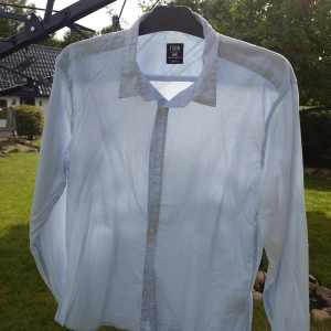 Ljusblå skjorta från FSBN, slim fit - Ljusblå skjorta från FSBN i slim fit-modell. Klassisk krage, knäppning framtill och långa ärmar. Skjortan är tillverkad i bomull och har en stilren, enkel look som passar perfekt till jeans eller chinos.