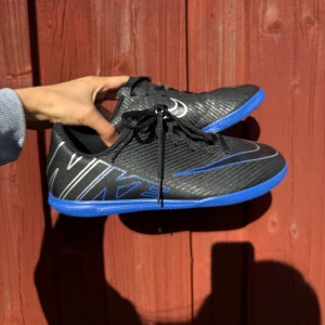 Nike svarta och blå fotbollsskor - Svarta & blå futsalskor – nästan oanvända Säljer ett par futsalskor/inomhusfotbollsskor, använda endast 2-4 gånger så de är i nyskick. 	•	Storlek: [38] 	•	Färg: svart & blå 	•	Nypris: 600 kr – säljes för [400 kr]  Perfekta för inomhusfotboll/futsal. 