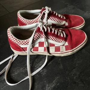 Rödvita rutiga Vans sneakers - Säljer ett par klassiska Vans sneakers i rödvitt rutigt mönster. Skorna har vit sula, snörning och den ikoniska sidoremsan. Ovandelen är i mocka och textil, med coola rutiga detaljer och kontrasterande vita sömmar. Perfekta för en streetstyle-look.